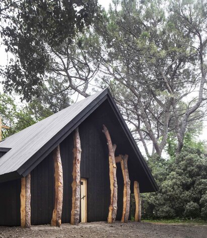 Eine kleine Kapelle aus dunklem Holz umgeben von Bäumen | © Alessandra Chemollo