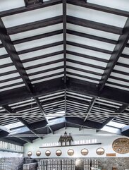 Die Dachstruktur aus Holz einer großen Produktionshalle mit dunkel lackierten Leimbindern, Pfetten und Sparren | © Benjamin Pfitscher