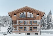 Ein Gebäude umgeben von Schnee; auf drei verputzten Geschossen thront ein neues Dachgeschoss mit Außenverkleidung aus Holz | © Davide Perbellini