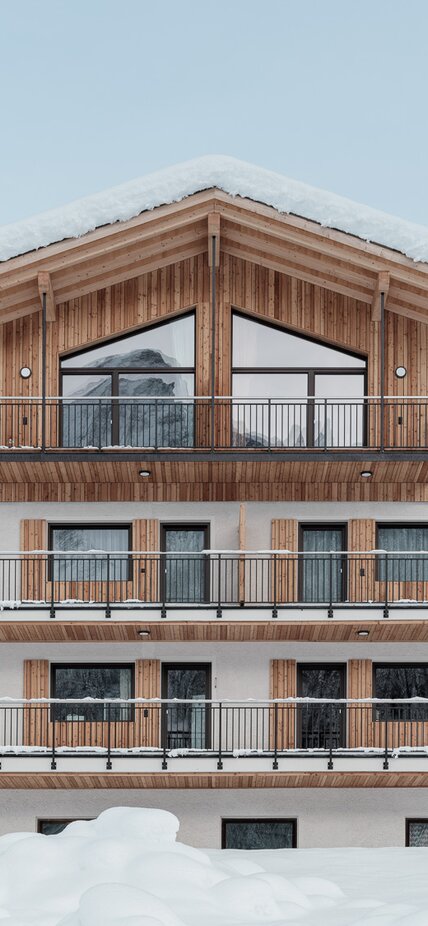 Ein Gebäude umgeben von Schnee; auf drei verputzten Geschossen thront ein neues Dachgeschoss mit Außenverkleidung aus Holz | © Davide Perbellini