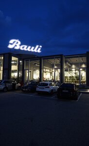 Eine Autobahnraststätte in der Nacht mit großen Glasflächen, auf dem Dach steht der Schriftzug "Bauli"