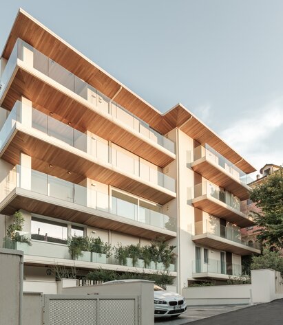 Un edificio residenziale a più piani con parapetti dei balconi in vetro e intradossi dei balconi e del tetto in legno | © Davide Perbellini