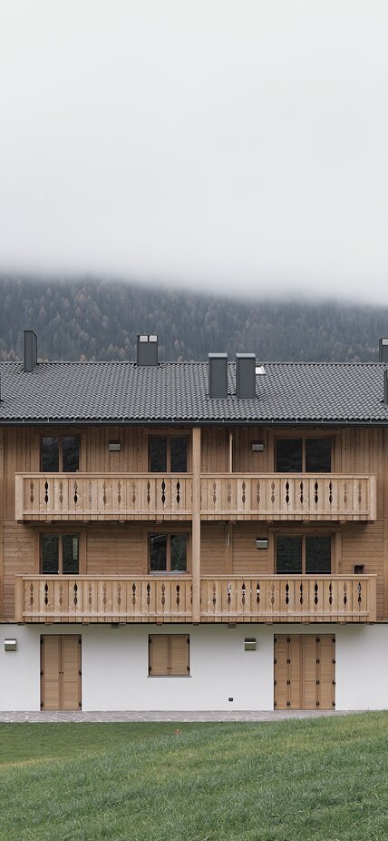 Ein dreistöckiges Gebäude mit einer verputzten Fasssade im Erdgeschoss und Fensterläden aus Holz, die zwei Obergeschosse und die Balkone sind aus naturbelassenem Holz | © Davide Perbellini