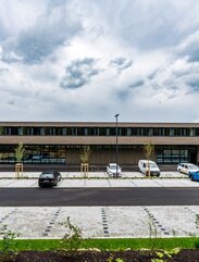 Ein breites zweistöckiges Gebäude mit einer Fassadenverkleidung aus Holzleisten, davor ein Parkplatz | © Roland Wehinger